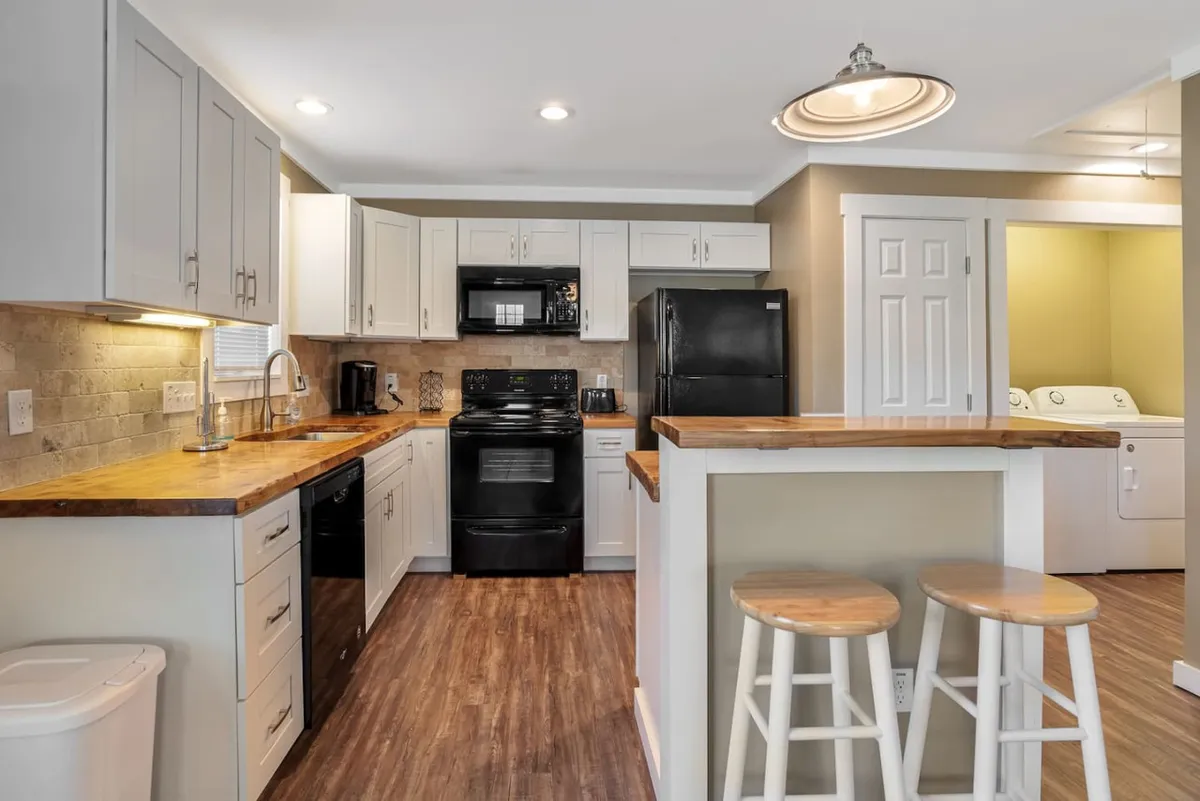 A modern kitchen interior featuring a wooden countertop island, sleek black appliances, and an inviting, functional layout. The space is well-lit and designed for both cooking and gathering, evoking a sense of comfort and utility.
