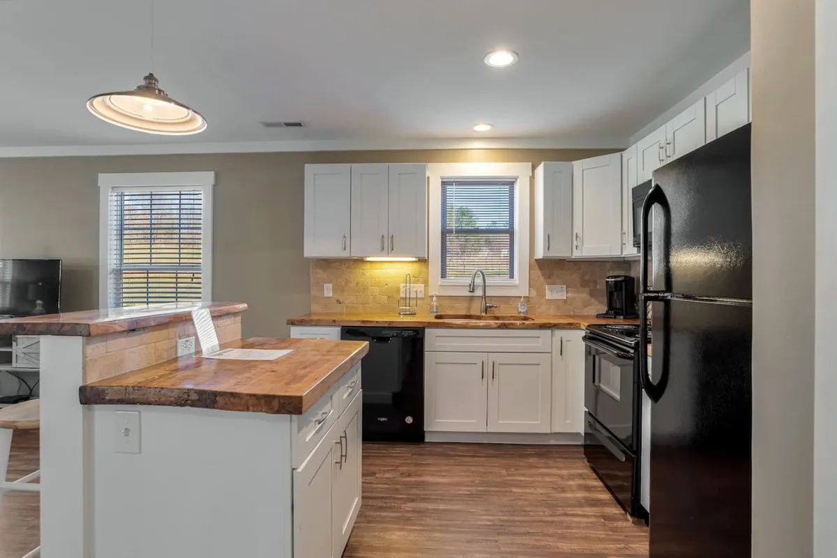 This image features a spacious kitchen with a central island, gleaming stainless steel appliances, a bright window that lets in ample natural light, and crisp white cabinetry. The scene exudes warmth and highlights the kitchen's modern comforts, making it ideal for both everyday cooking and special gatherings.