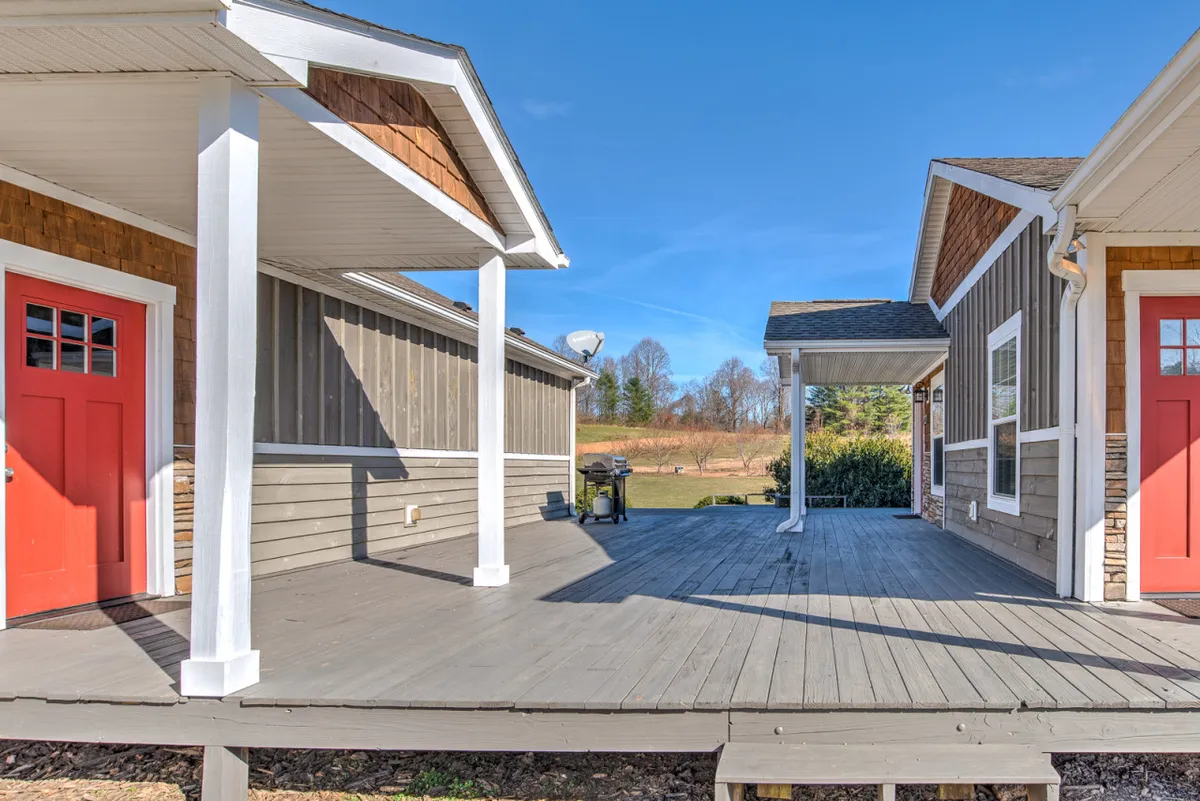 This image displays the exterior of Traveler's Haven, focusing on eye-catching red doors, a spacious wooden deck, and the surrounding landscape. The deck appears inviting, with ample space for guests to sit and relax while enjoying the natural scenery.
