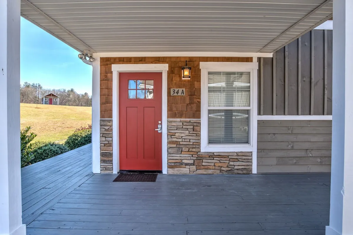 The home’s inviting exterior featuring a bold red front door set against a backdrop of stone and wood accents, with a window showing hints of the interior’s warmth. The approach promises a private, welcoming entrance.
