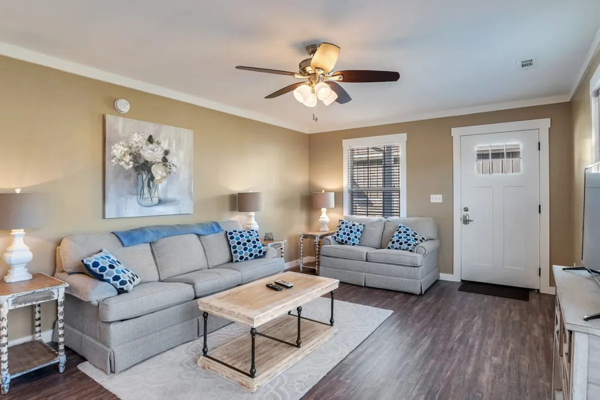 A cozy living room with a plush sofa and soft throw pillows sits at the center, anchored by a warm wooden coffee table. Tasteful artwork adorns the walls, and a gentle lamp casts a soothing glow over the space, inviting guests to unwind. The setting is perfect for relaxing with a book, sharing coffee and conversation, or enjoying a relaxing movie night.