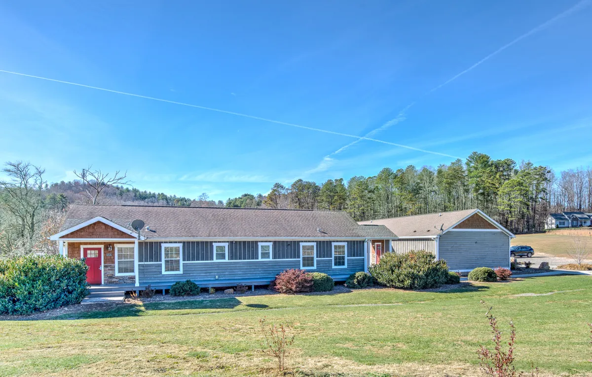 The exterior shot features the red front door, blue-gray siding, and abundant greenery encircling Traveler's Haven. The image conveys a private, serene environment, ideal for a peaceful retreat, and suggests nearby scenic views over hills and opportunities to enjoy local wildlife.